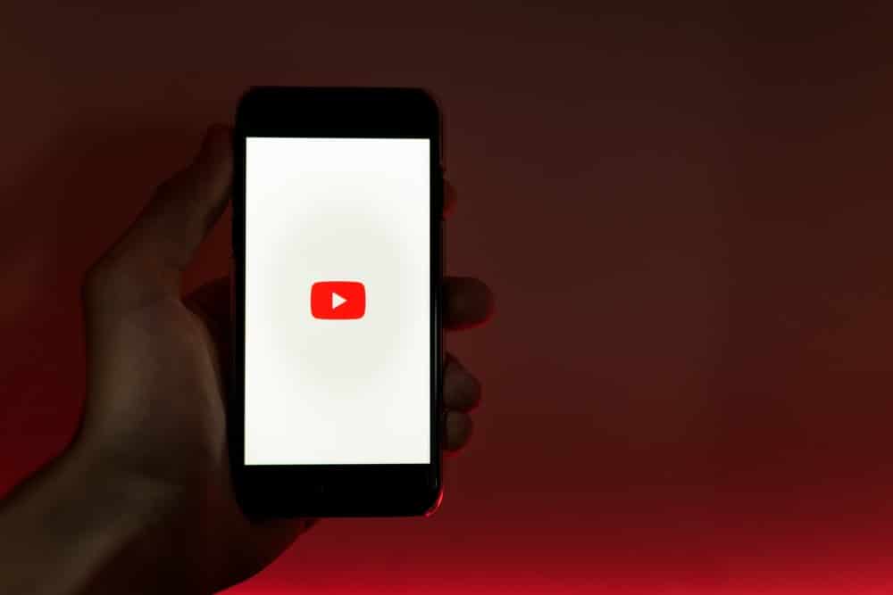 eliminar lista de reproduccion de youtube, una mano alzada en una habitacion oscura tiene la pantalla de inicio de youtube