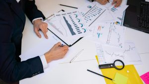 Dos personas analizando documentacion con infografías sobre una mesa blanca en un ambiente profesional.