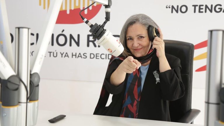 una mujer señala a la camara con el dedo indice mientras te pone unos cascos en las orejas, se encuentra en una sala de conferencias ya que hay un microfono de los que salen en la television
