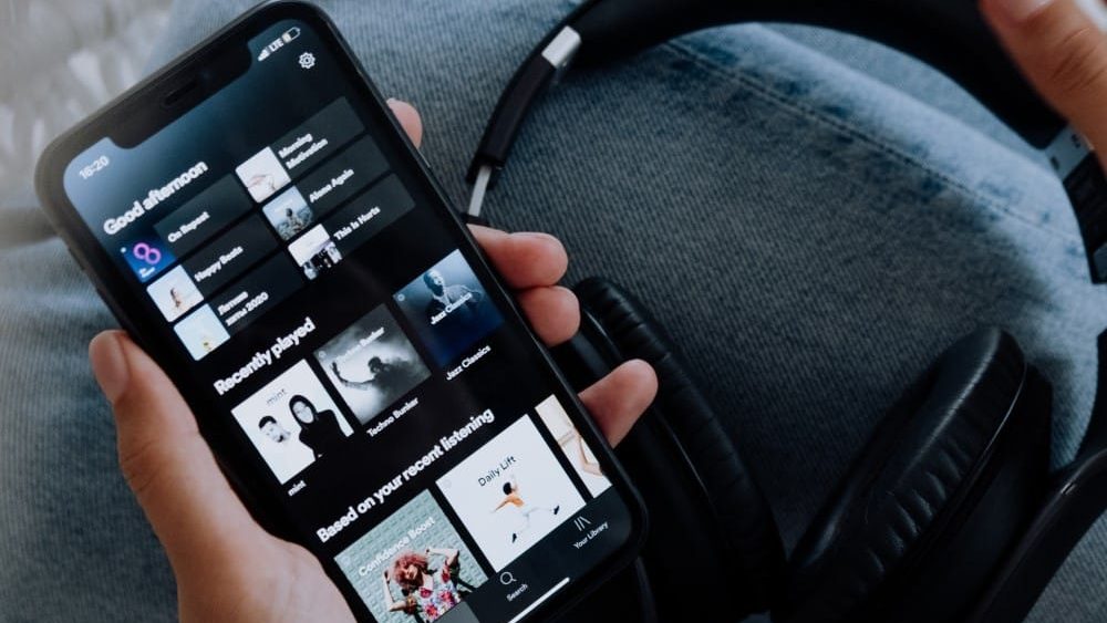 eliminar cuenta de spotify, una persona usa un movil en el cual se ve la pantalla de inicio de spotify, en la imagen tambien se ven unos cascos