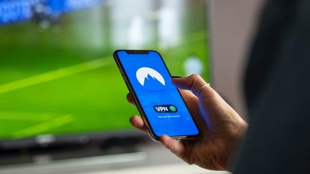 que es una vpn, una persona sujeta un movil donde hay una pantalla que pone VPN, hay una pantalla de tele detras