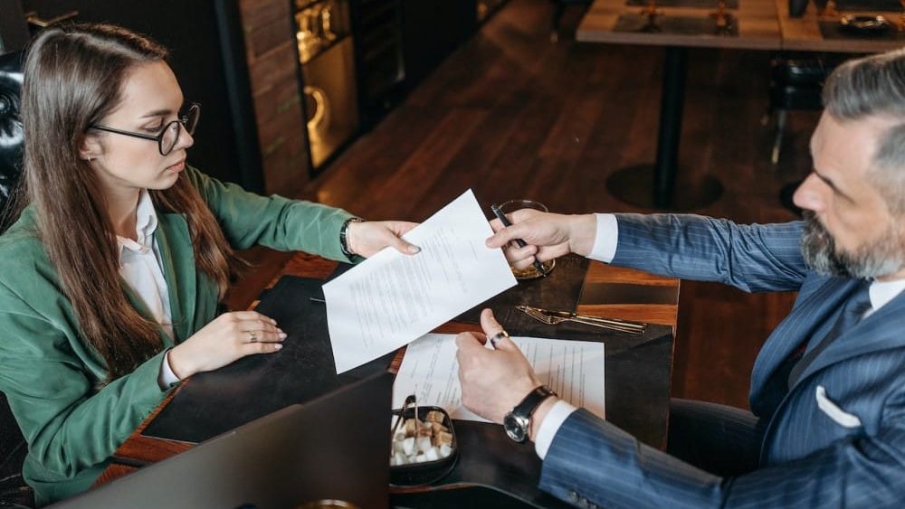 aepd, dos personas en una reunion de trabajo, una le entrega documentacion a la otra