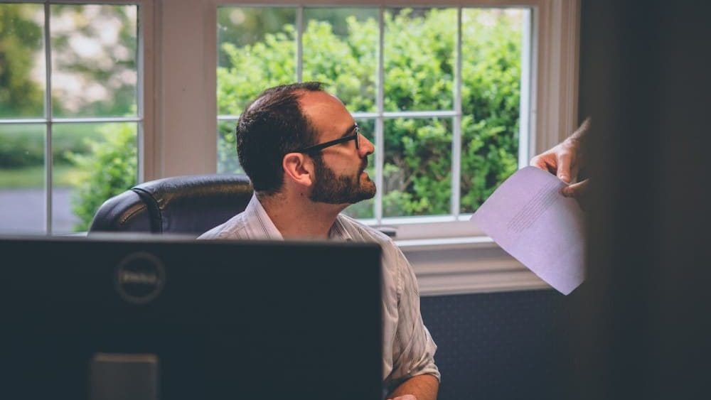 que es un business angel, una persona le enseña o le entrega documentacion a un hombre que esta en una oficina frente a un ordenador el cual se ve en primer plano