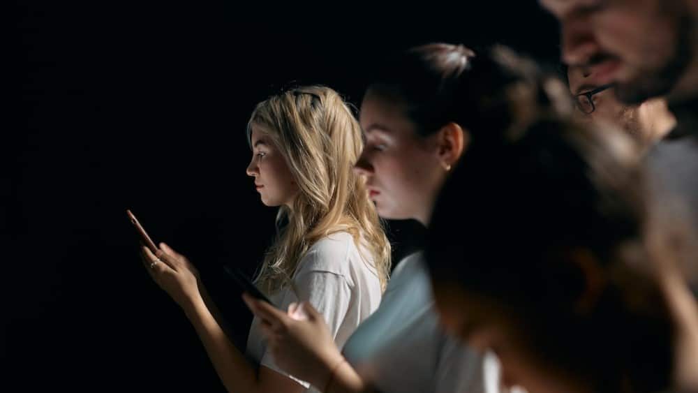 empantallados, se ven a un grupo de jovenes mirando el movil con un fondo oscuro