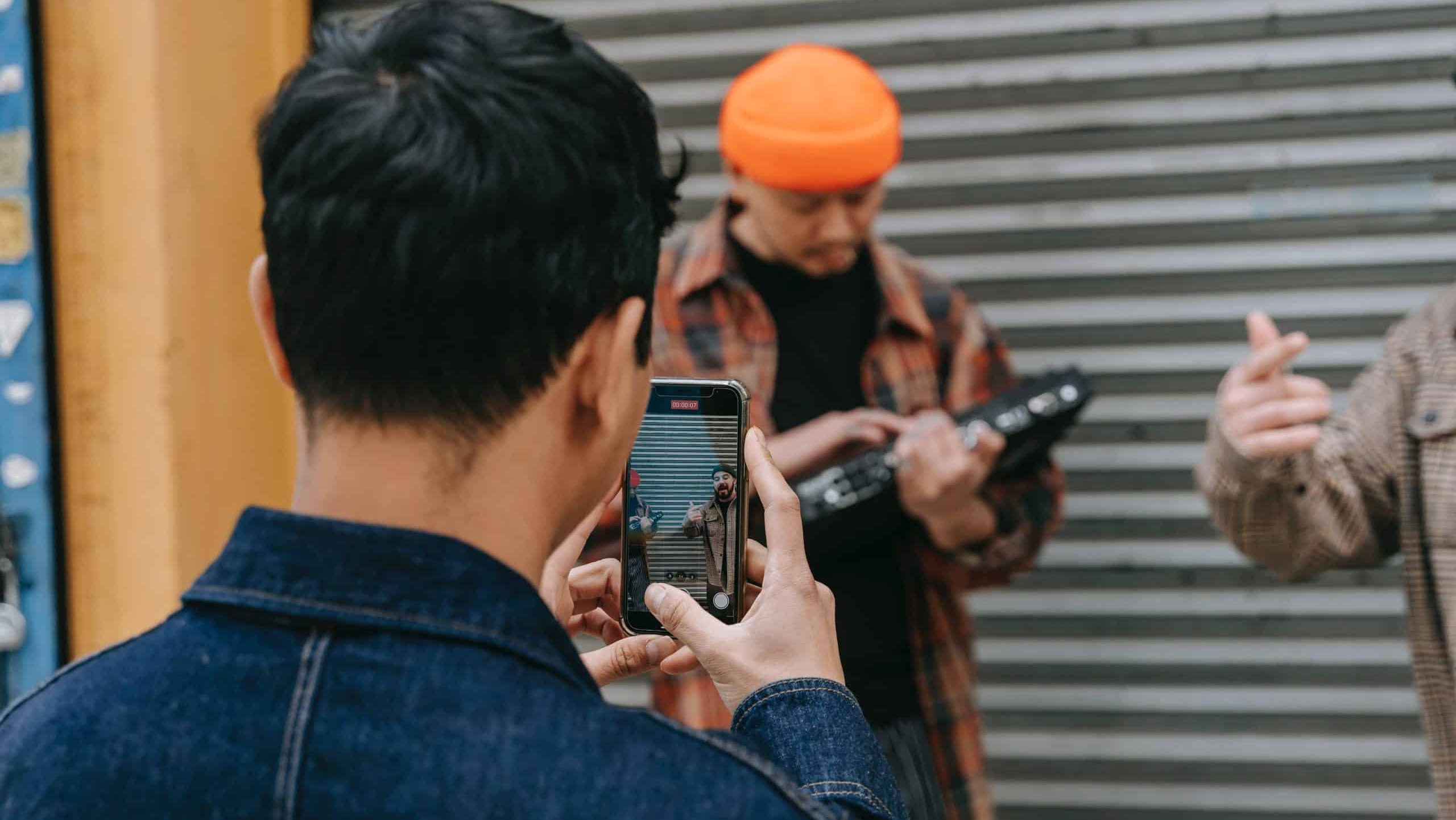 una persona graba a otras dos con el movil, estas dos personas que son grabadas estan componiendo algo musicalmente o eso parece ya que hay uno con un instrumento electronico como una tabla de dj cogidas en las manos y el otro chico esta cantando
