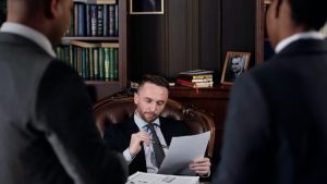 que es un term sheet, 3 abogados o hombres de negocio estan en una reunion infromal, pues 2 estan de pie y el otro esta sentado, mirando un docuemtno y con la patilla de las gafas en la boca, estil pensativo