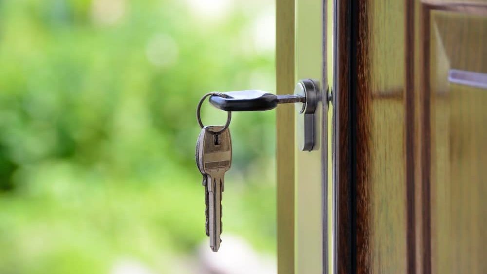 que es un usufructo, unas llaves estan colgadas y puestas en una cerradura de una puerta de madera, en el fondo se puede observar verde de arboles, maleza o arbustos