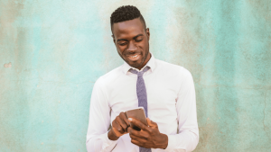 una persona con camisa y corbata usa un movil, detras tiene una pared verde desgastada