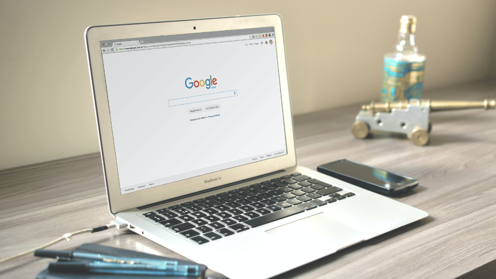 se ve un portatil macbook air en una mesa de madera que tiene abierto safari con la busqueda de google