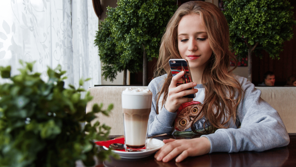chica con un cafe en una cafeteria usando el movil