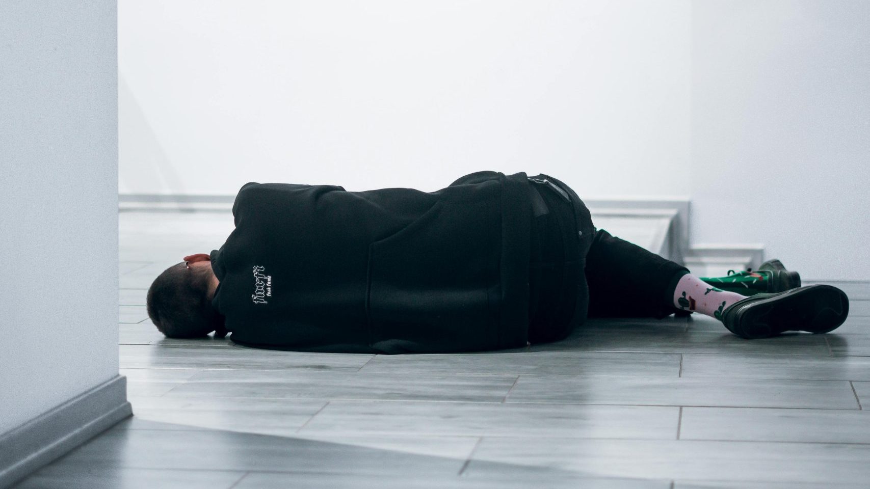a woman is on the floor, laid down, and facing the wall in the background. Therefore, we cannot see her face