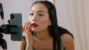 girl recording herself with a tripod, she has lipstick on and is wearing a dress