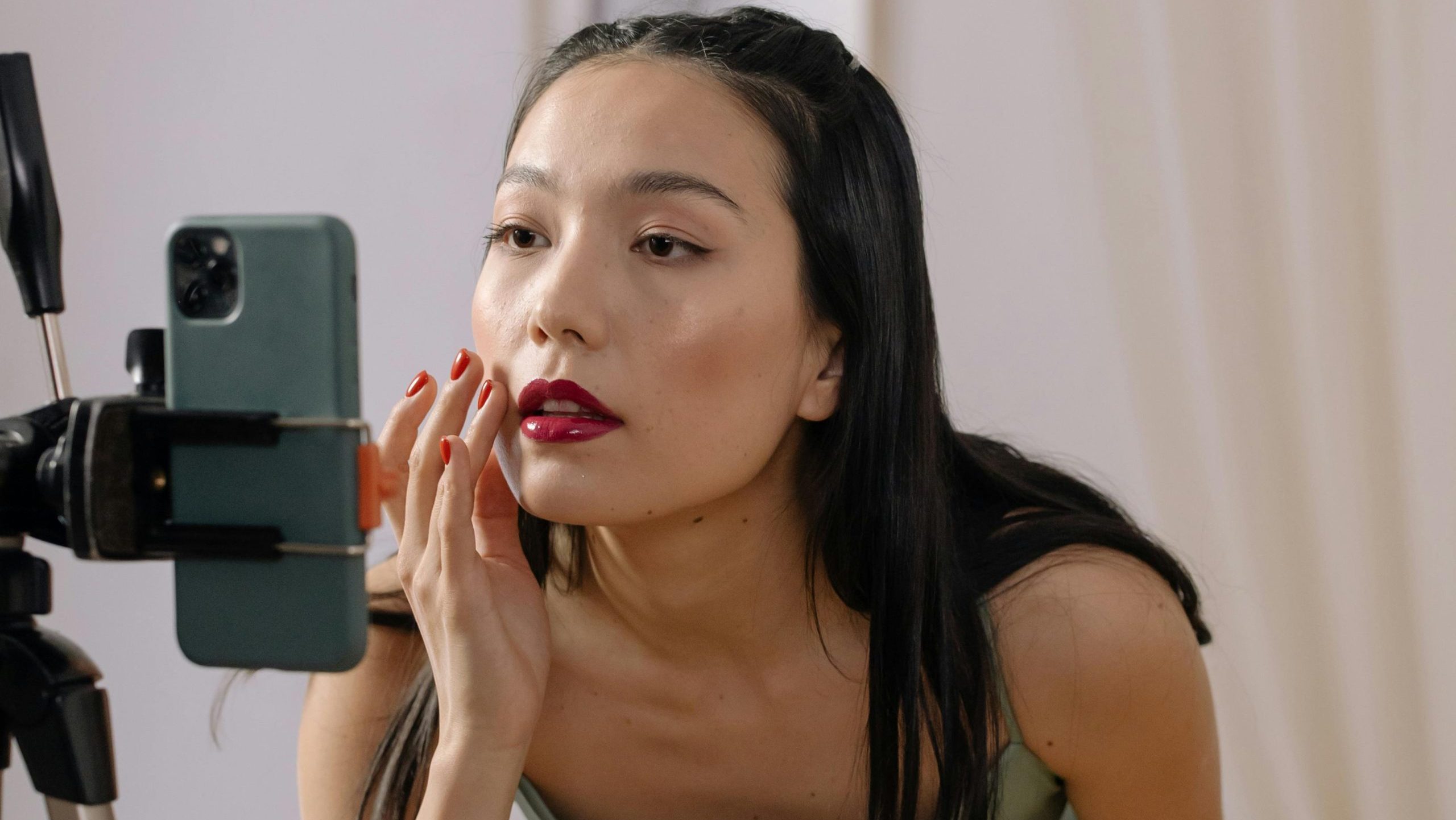 girl recording herself with a tripod, she has lipstick on and is wearing a dress