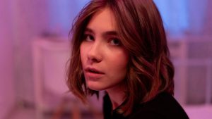 girl with a neutral expression in a blurry room, the light is purple