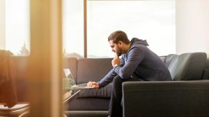 Man sitting on a living room sofa using a computer with an expression