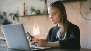 girl using cell phone in front of laptop, warm atmosphere