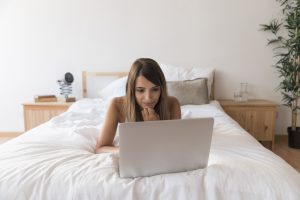 una chica tumaba bocarriba mirando el portatil en la cama, el ambiente es muy calido