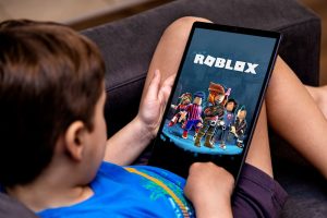 Boy plays Roblox on a tablet on a black sofa