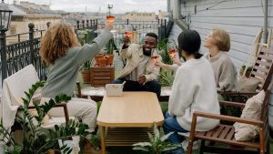 4 personas alzan una copa de vino rosado en la terraza del piso mas alto de un bloque, rostros felices, ocurre en una ciudad. Encuentro de meetup