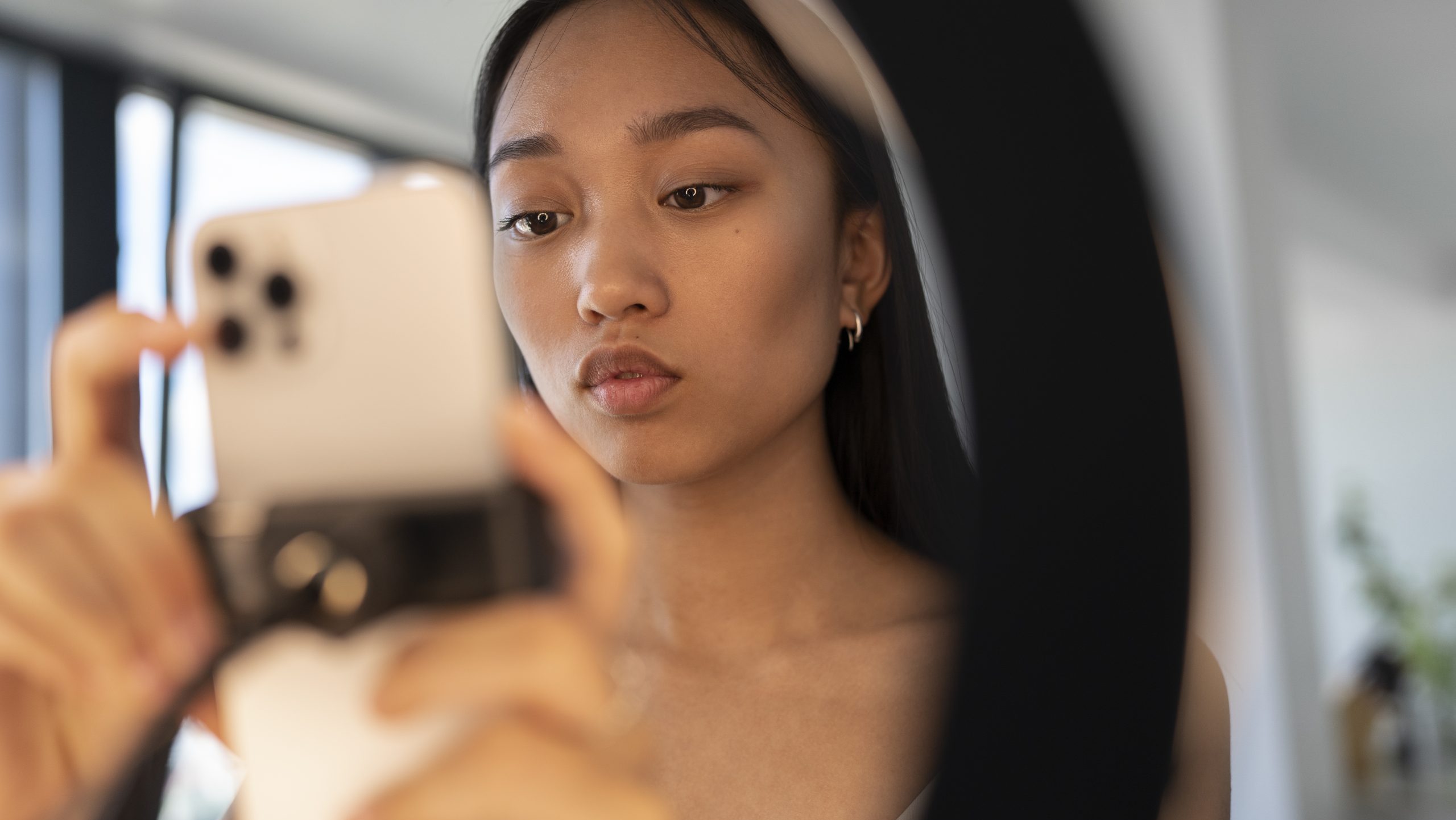 A girl is looking at her mobile phone while it's on a tripod. The focus is on her face, as the rest of the image is out of focus.