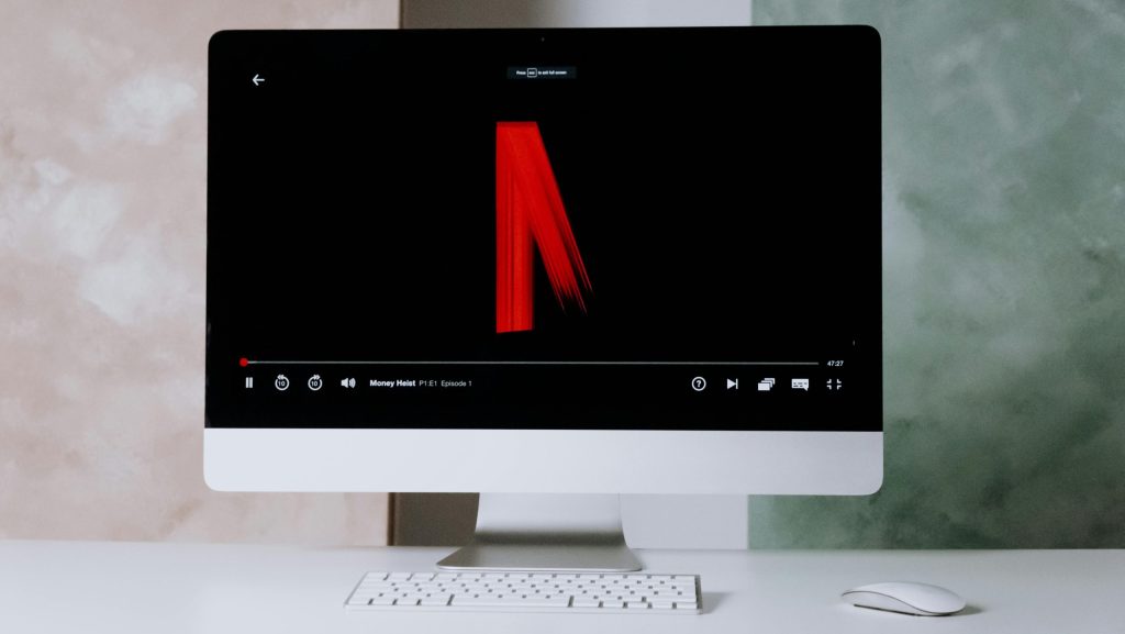 el fondo es blanco, la imagen es toamada a un imac con teclado y raton, en la pantalla se observa el logo de netflix cuando comienza una serie