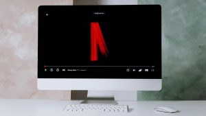 el fondo es blanco, la imagen es toamada a un imac con teclado y raton, en la pantalla se observa el logo de netflix cuando comienza una serie