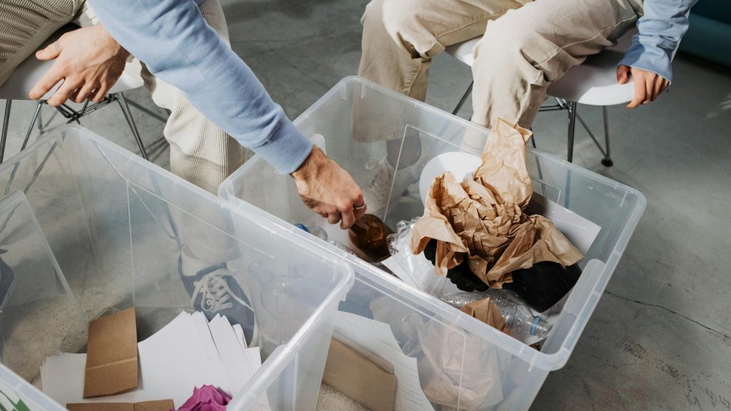 dos personas vestidas con los mismos colores en las prendas estan sentadas en sillas, su rostro es desconocido, ordenan basura en dos cajas de plastico