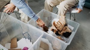 dos personas vestidas con los mismos colores en las prendas estan sentadas en sillas, su rostro es desconocido, ordenan basura en dos cajas de plastico