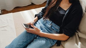 Una mujer joven sentada en un sofá usando un smartphone.
