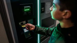 un chico inserta tarjeta de credito en un cajero automatico de noche, el ambiente se siente sospechoso o peligroso