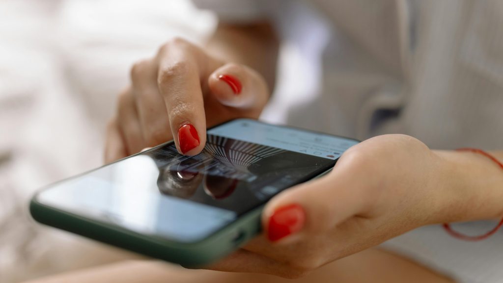 Mano de mujer con las uñas pintadas de rojo usando un teléfono móvil.